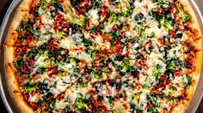 Close-up of a freshly baked pizza topped with broccoli, sun-dried tomatoes, olives, and melted cheese.