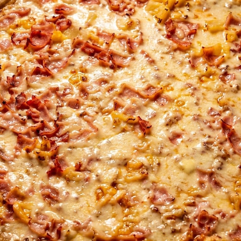 Close-up of a Hawaiian pizza with melted cheese, ham, and pineapple chunks.