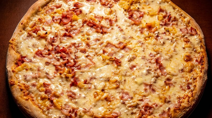 Close-up of a Hawaiian pizza with melted cheese, ham, and pineapple chunks.
